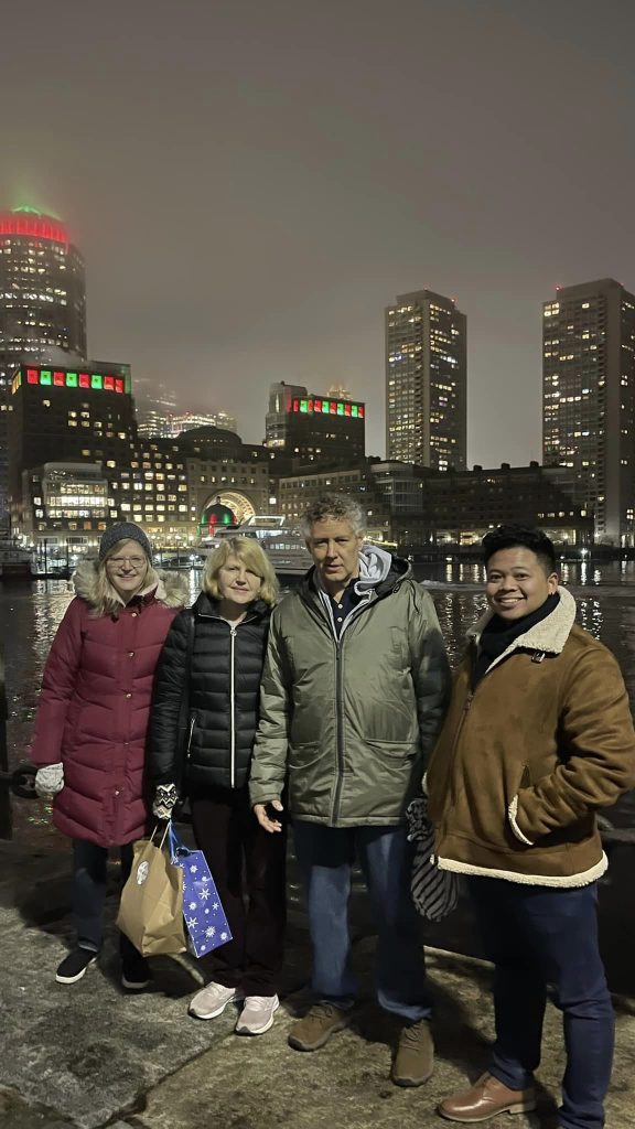 Gail Snow Moraski, Audrey Snow Barresi (Gail's twin sister), Jay Moraski (Gail's husband) and Nick Snow (Gail's niece) standing in Fan Pier area Boston MA with Rowe's Wharf and the Boston Harbor Hotel and Boston Harbor in background.